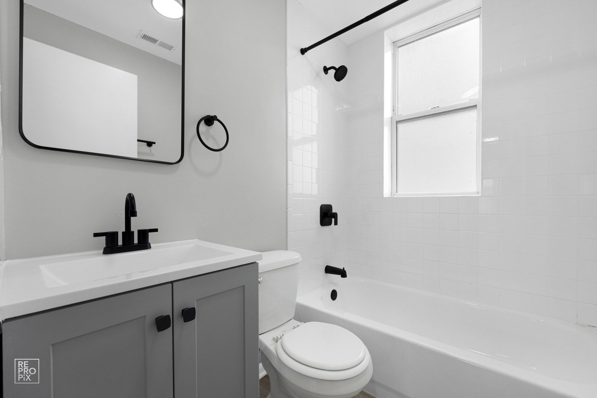 Bathroom with gray vanity, white toilet, and white tiled shower; black fixtures.