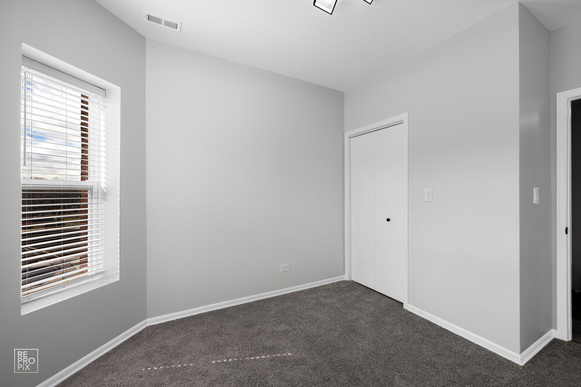 Empty room with gray walls, window with blinds, white door, and gray carpet.