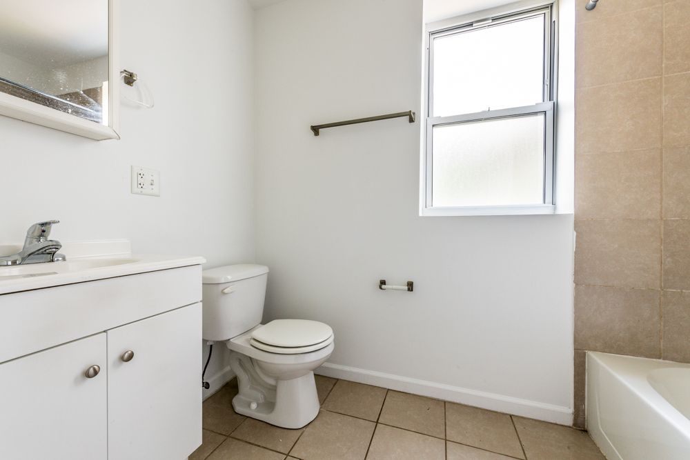 Bathroom with white walls, a sink, toilet, window, and a bathtub.