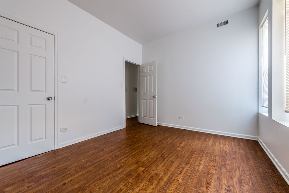 Empty room with wood-look floor, white walls, and two doors. Light comes from a window.