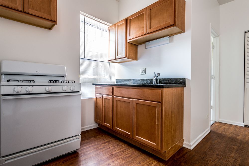 Kitchen with a white oven, wooden cabinets, a sink, and a window; hardwood floors.