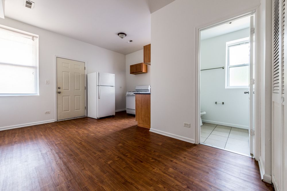Empty apartment interior: kitchen with refrigerator, cabinets, and entrance to the bathroom.