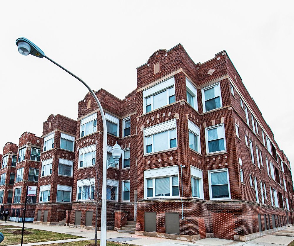Multi-story brick apartment building with white-trimmed windows and ornate details under a cloudy sky.