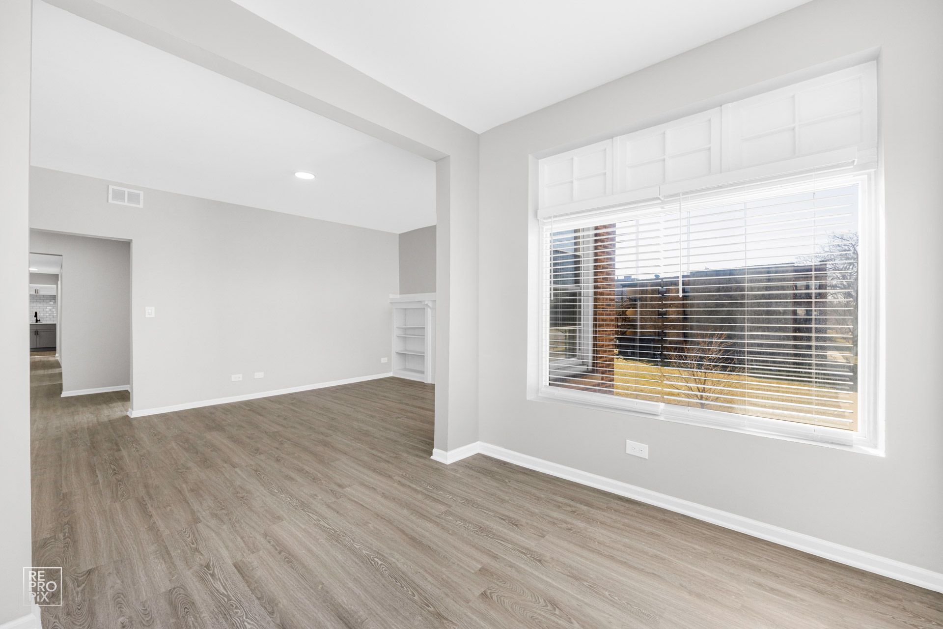 Empty room with large window, blinds, and hardwood-like flooring.