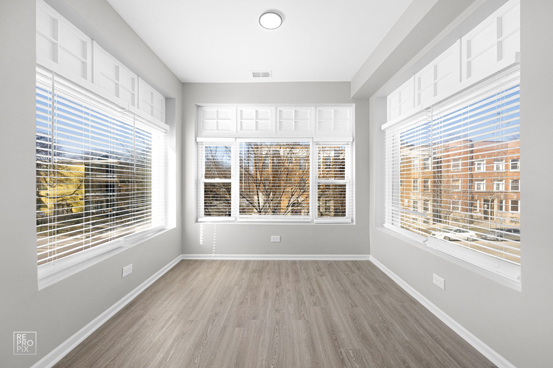 Empty room with three large windows, gray walls, and wood-look flooring.