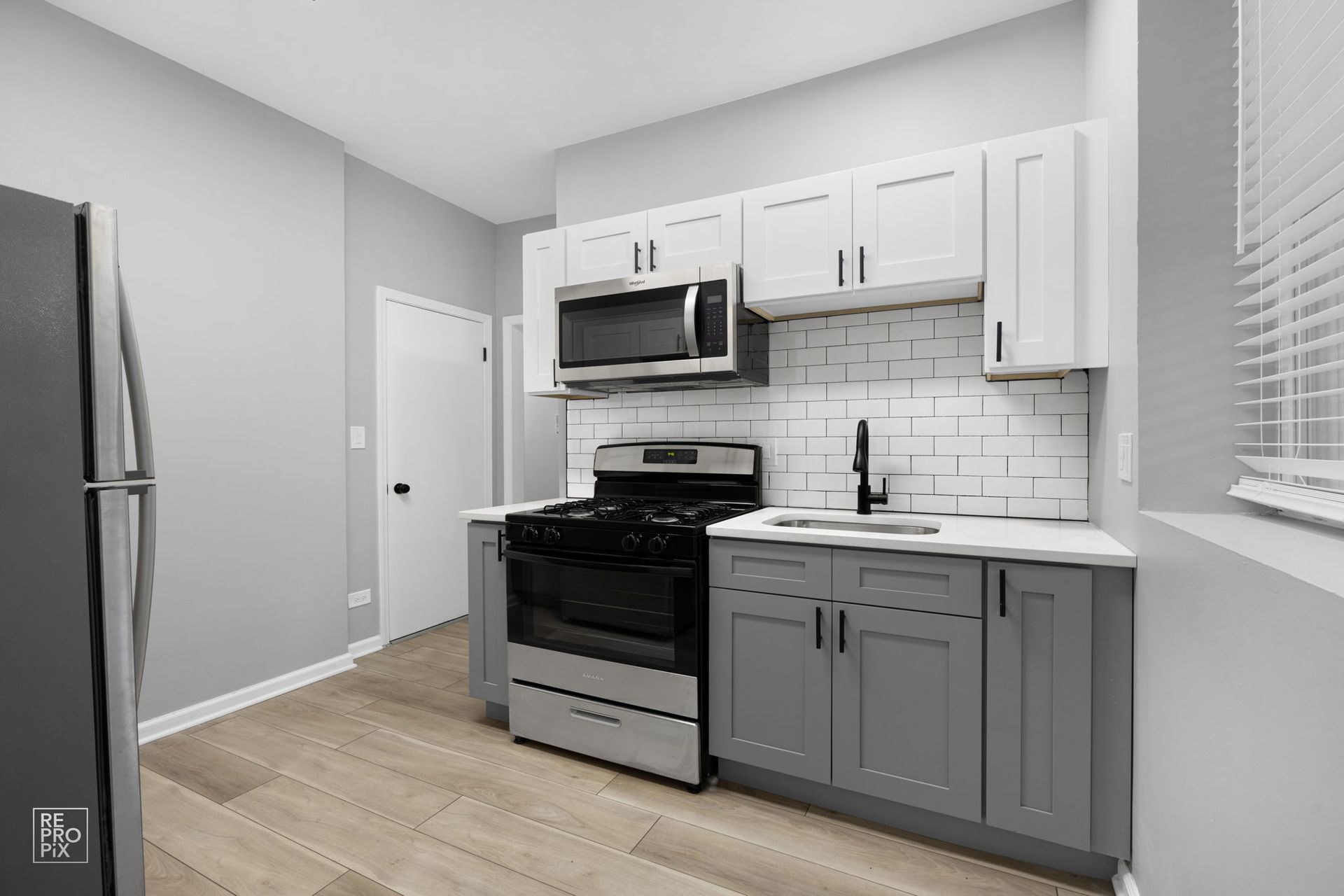 Modern kitchen with gray and white cabinets, stainless steel appliances, and subway tile backsplash.