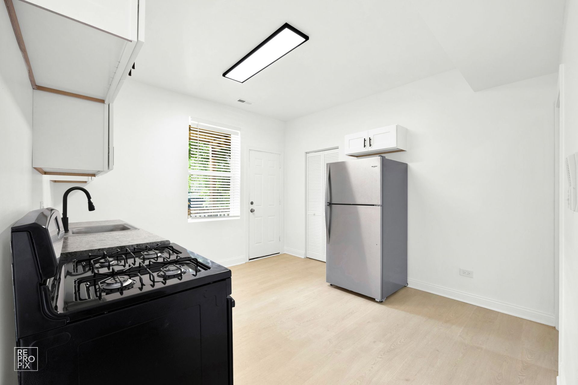 Small kitchen with a black stove, stainless steel refrigerator, and a window.