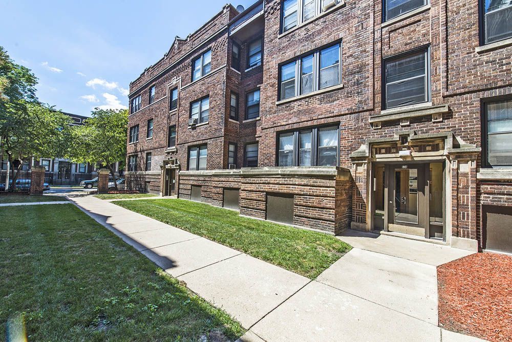 Brick apartment building with grass lawn and sidewalk.