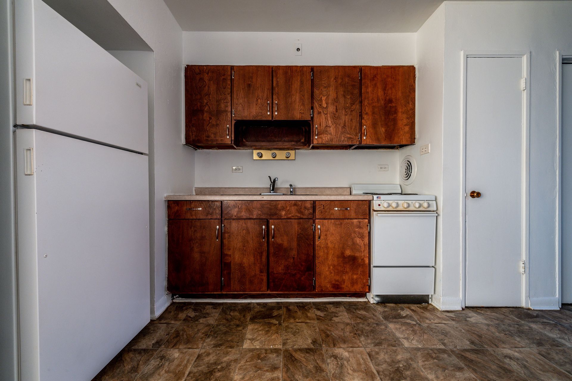 Small, empty kitchen with white appliances and dark wooden cabinets.