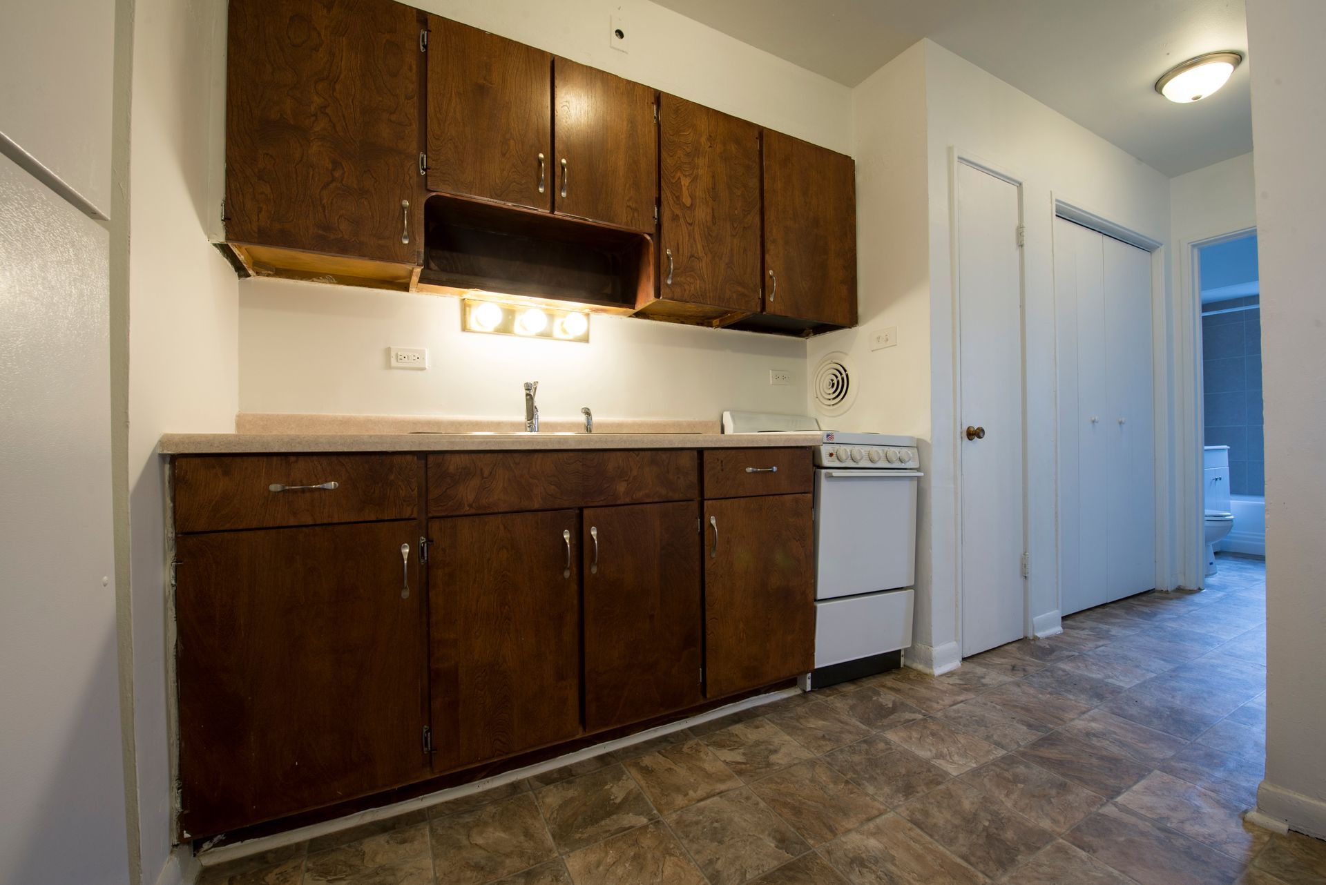 Kitchen with dark cabinets, white appliances, and linoleum flooring.