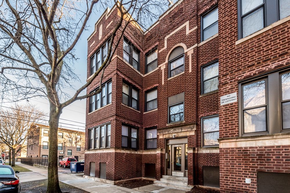Brick apartment building with dark trim and arched doorway on a city street.