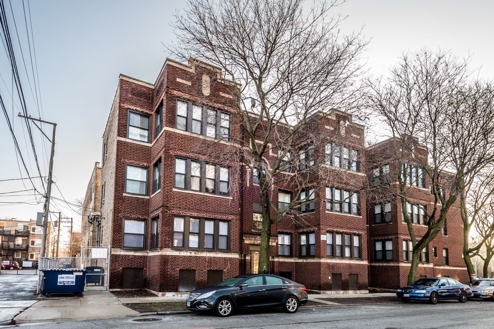 Brick apartment building on a city street, with cars parked out front and bare trees.