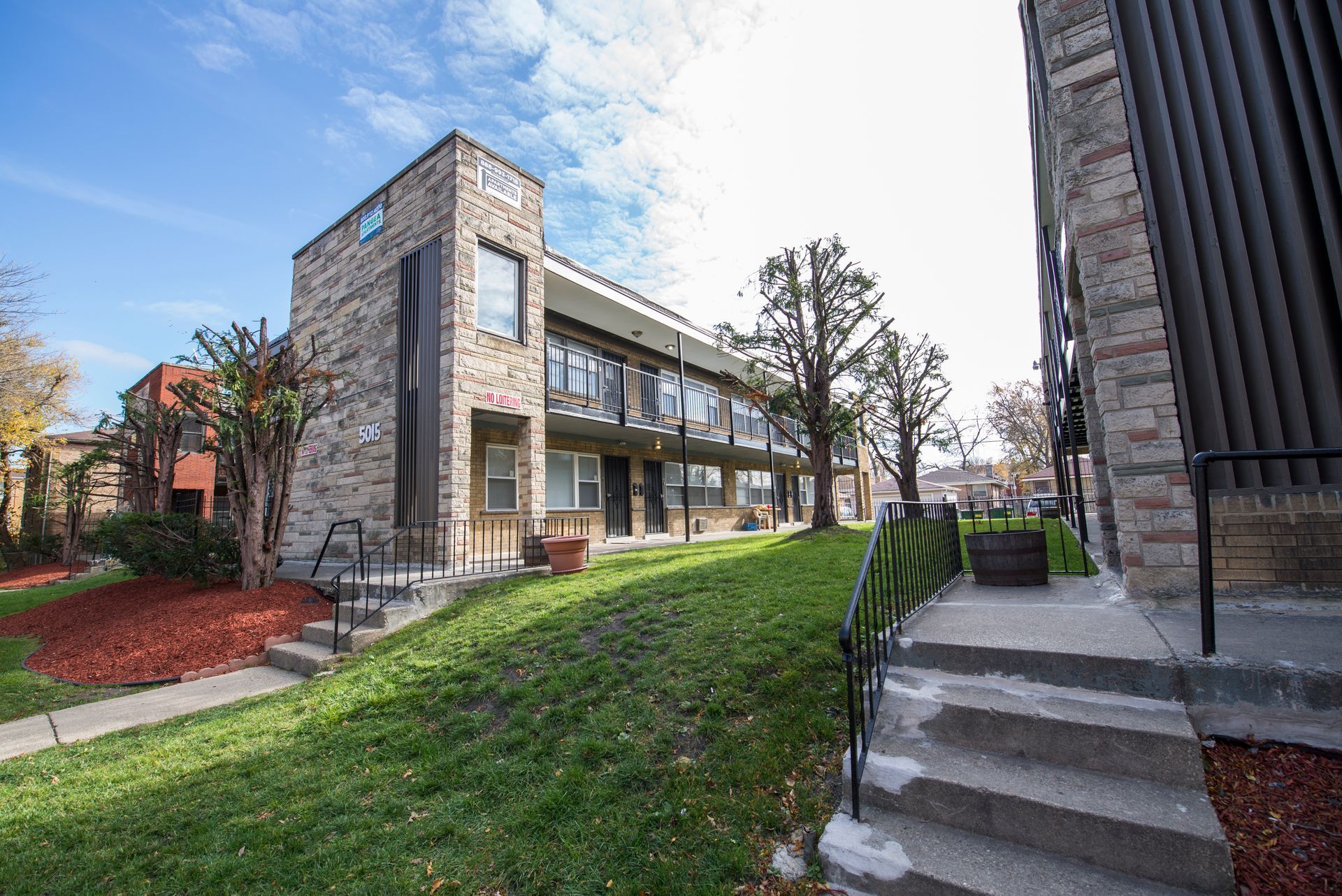 Two-story stone apartment buildings with grass lawn and blue sky.