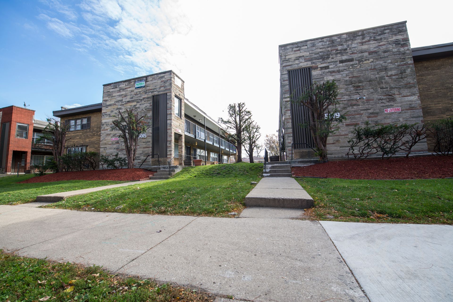 Buildings with stone and brick exteriors, grassy lawn, concrete pathway, and blue sky.