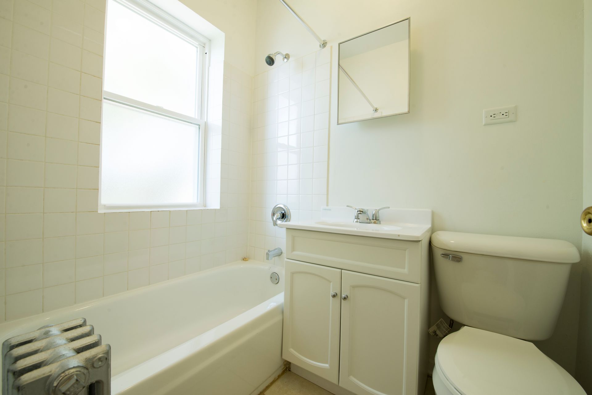 Bathroom with white tub, toilet, vanity, and small window. White tiled walls.