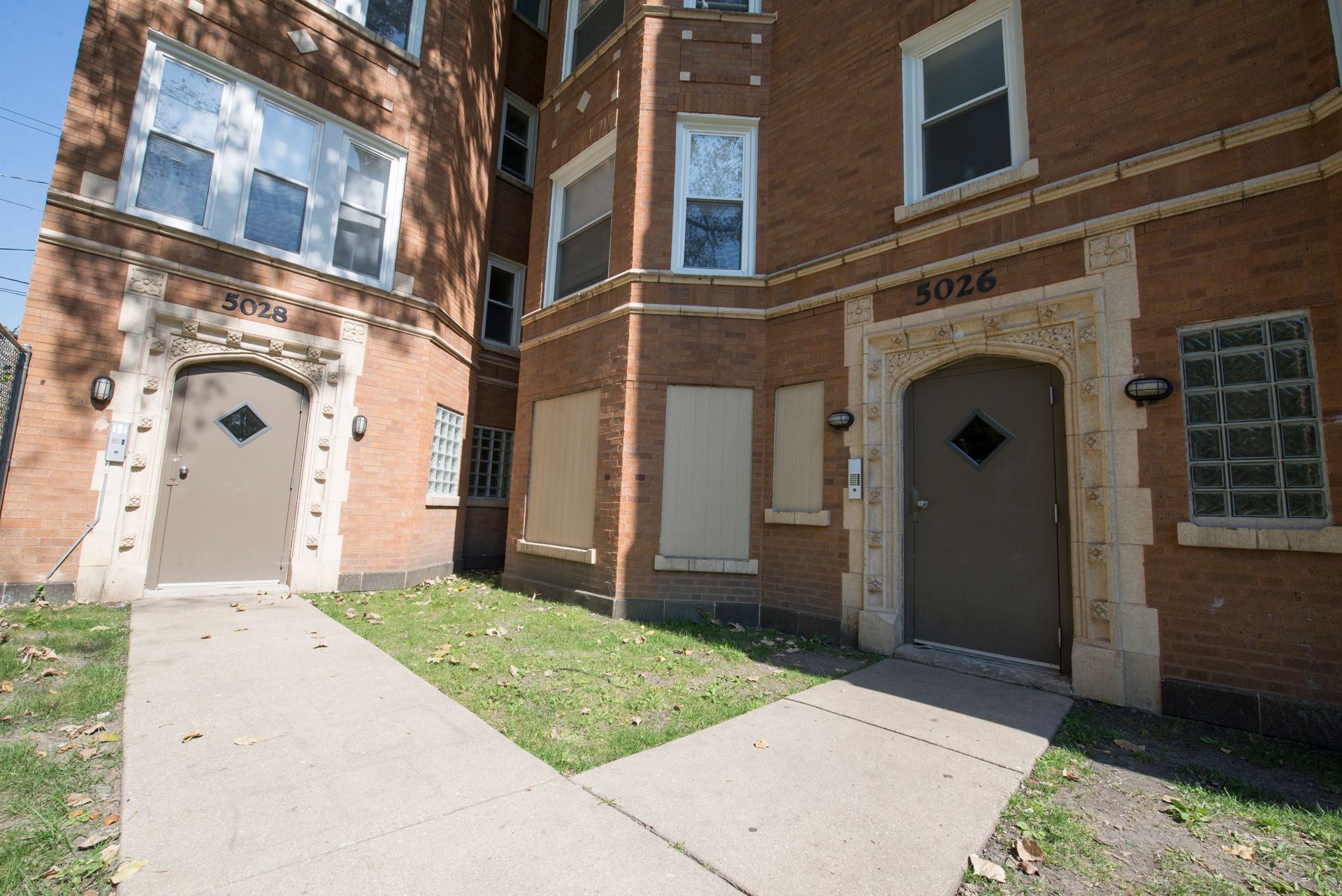 Brick apartment building with two arched entryways and a small patch of grass.
