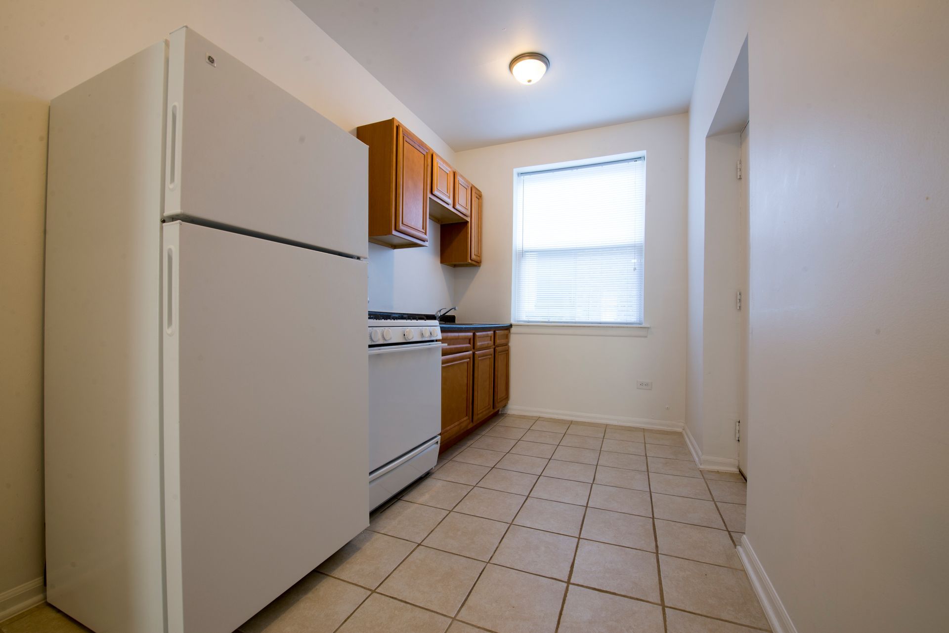 Kitchen with white appliances, brown cabinets, tiled floor, and a window.