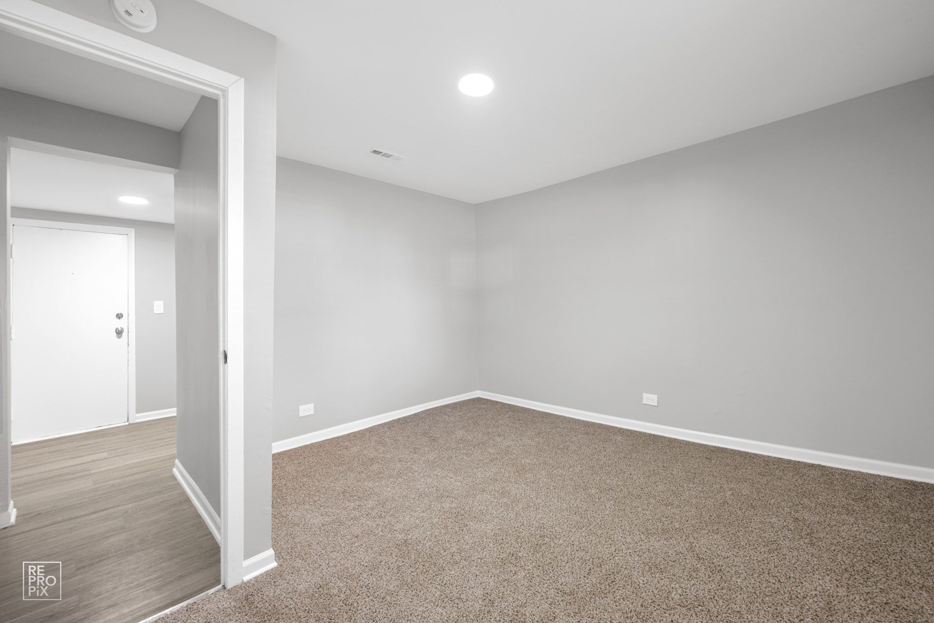 Empty room with gray walls, beige carpet, and doorway to a hallway with a white door.