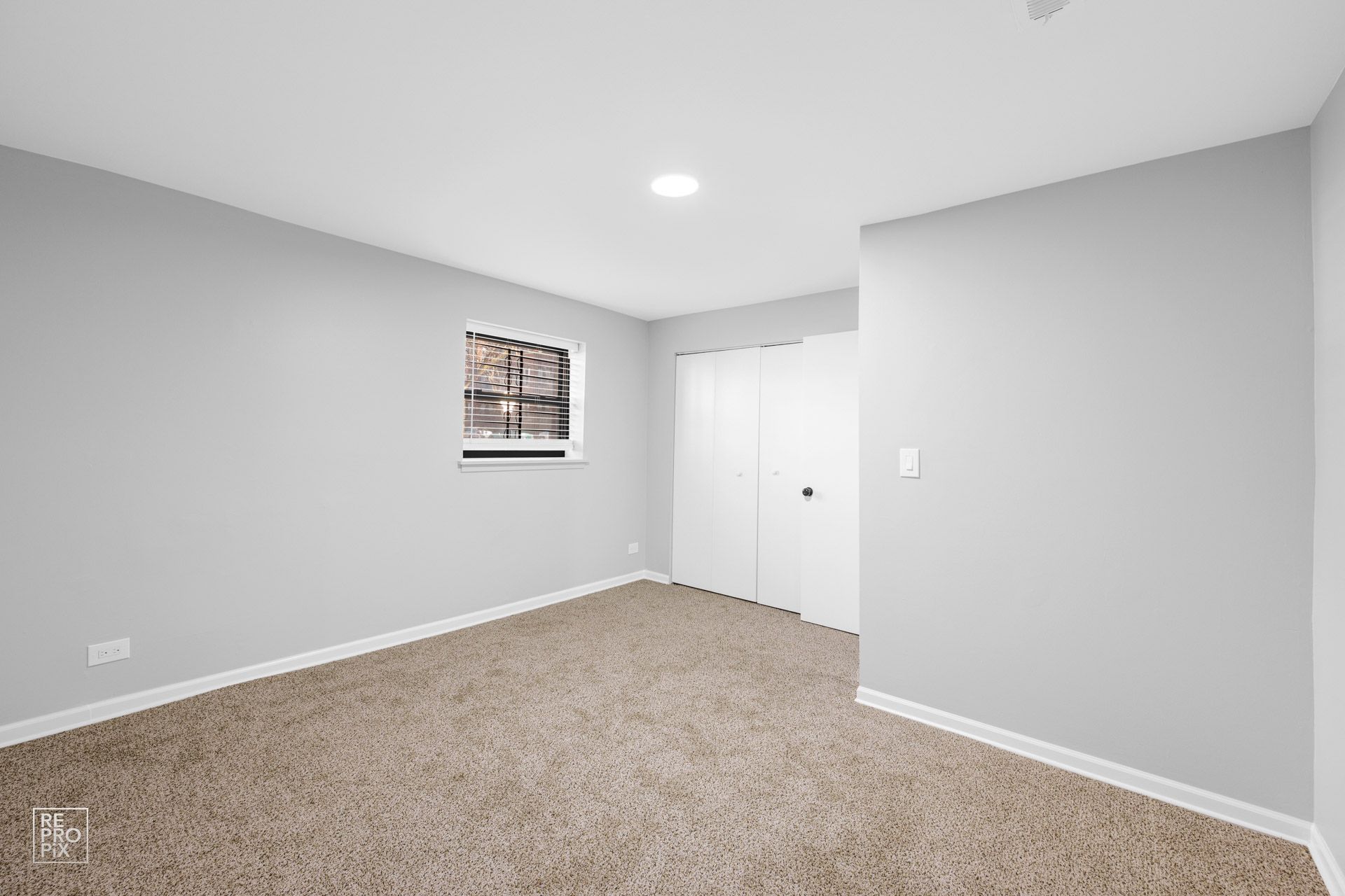 Empty bedroom with gray walls, carpet, window, and closet.