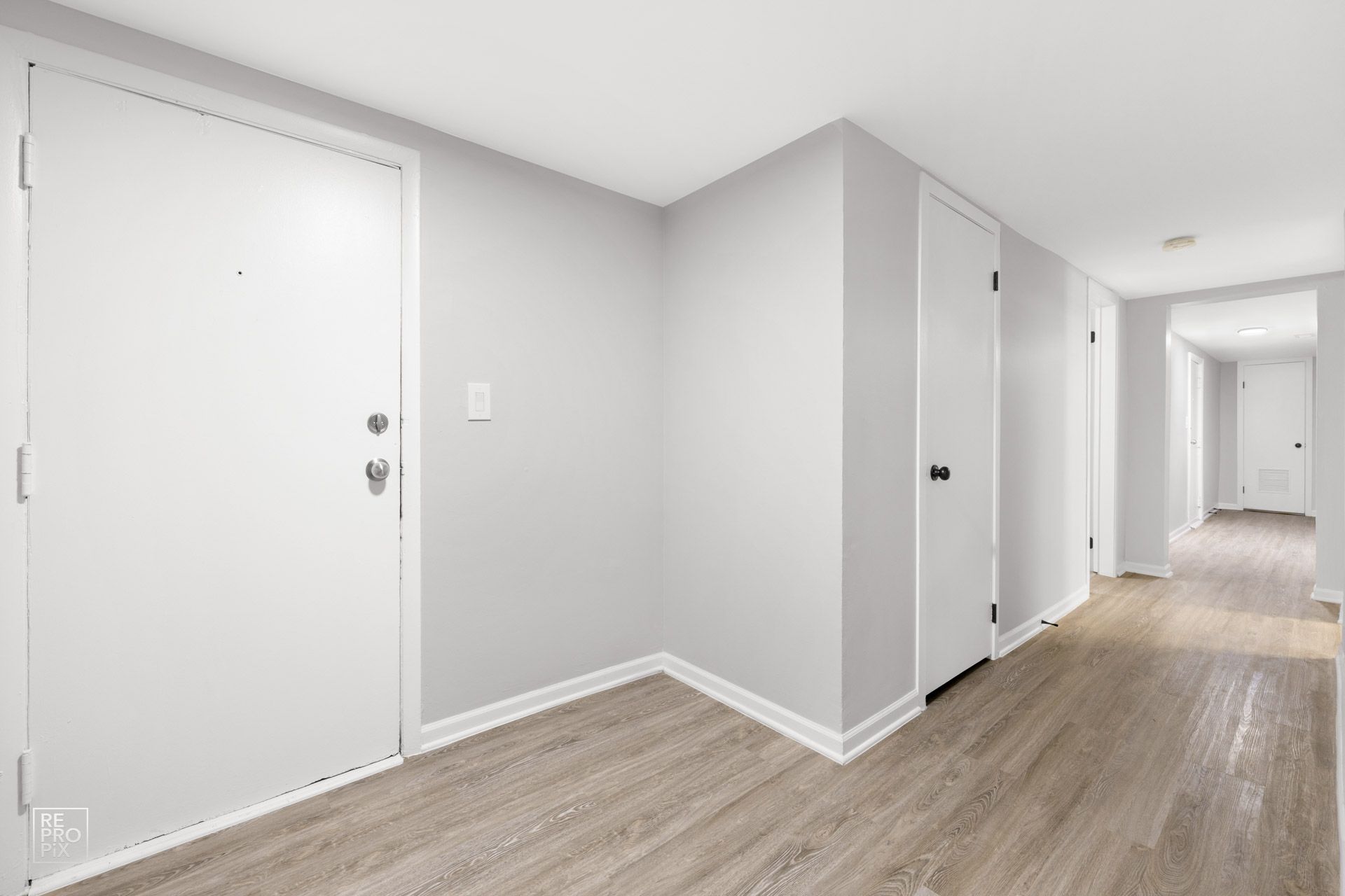 Hallway with white doors, light gray walls, and wood-look flooring.