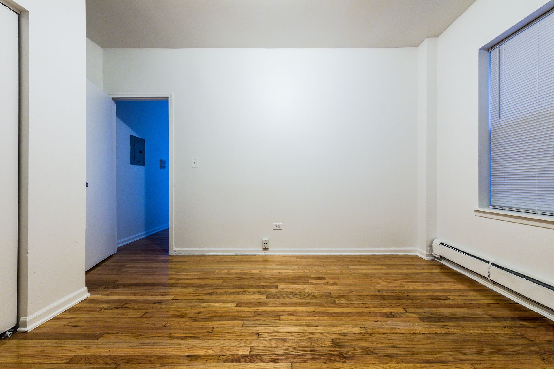 Empty room with hardwood floors, white walls, and a doorway. Window on the right.