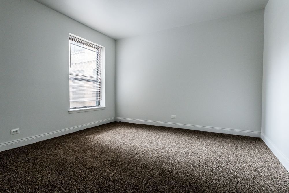 Empty room with brown carpet, white walls, and a window with blinds.