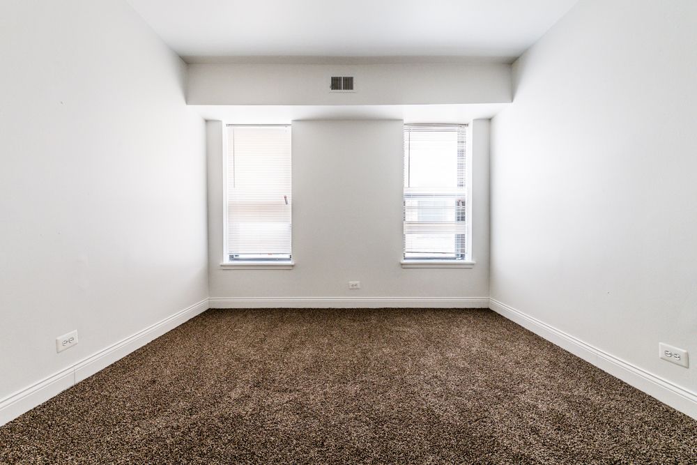 Empty room with brown carpet, two windows with blinds, white walls.