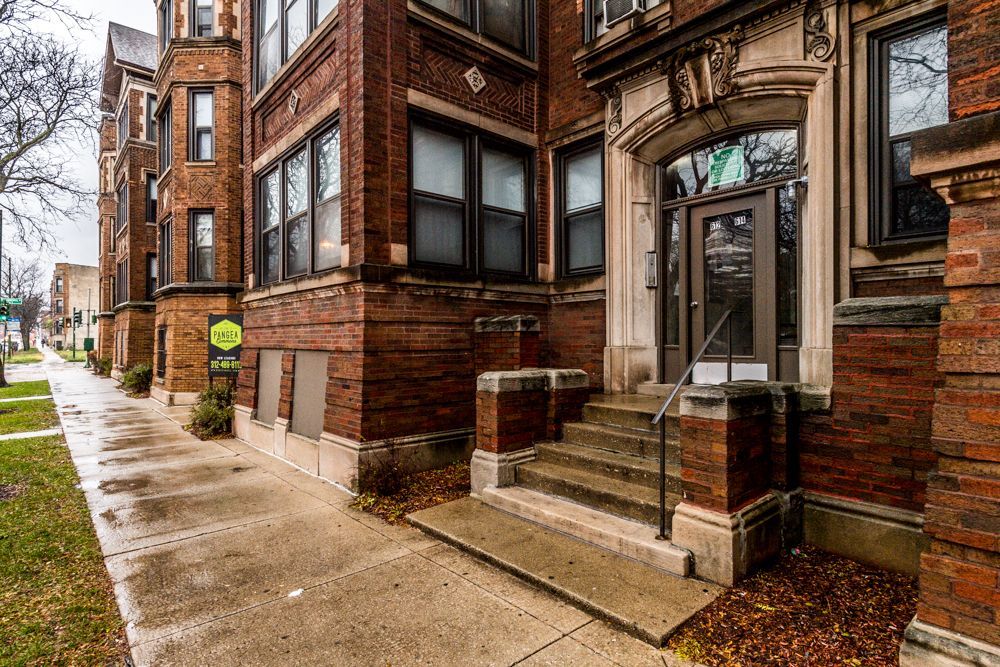 Brick apartment building with steps leading to a decorated entryway, and sidewalk.