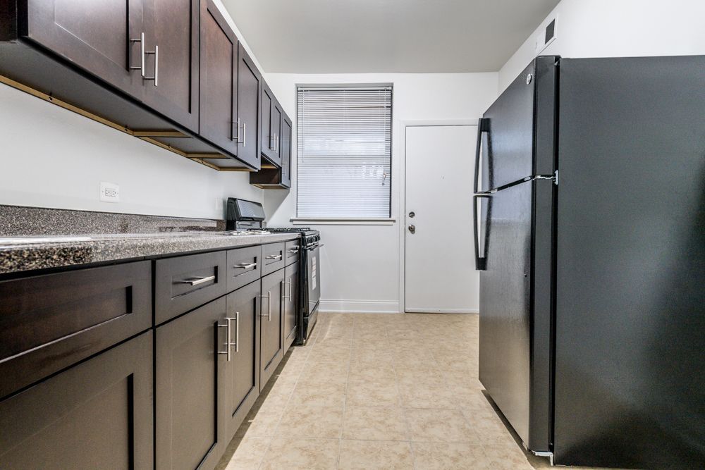 Kitchen with dark cabinets, gray countertop, black refrigerator, stove, window with blinds.