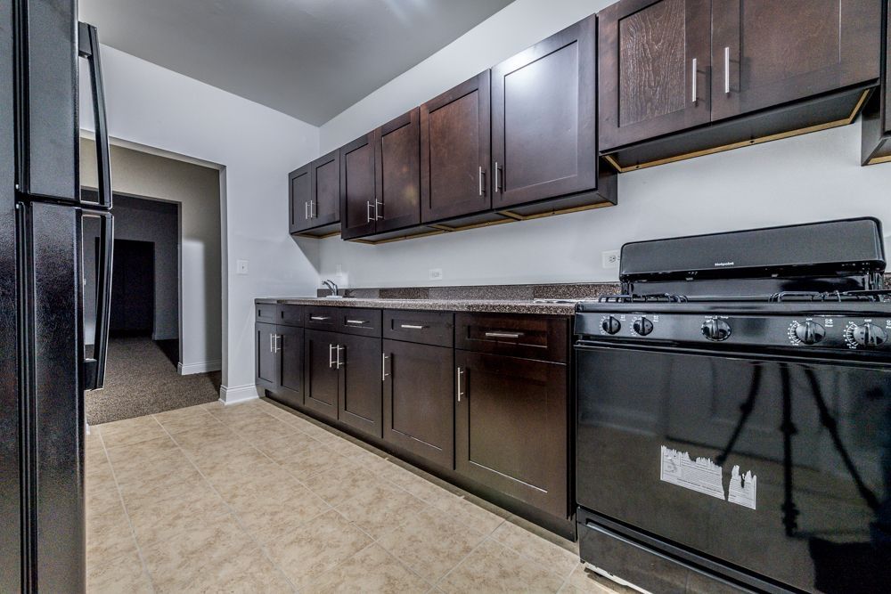 Kitchen with dark brown cabinets, black appliances, and neutral flooring.