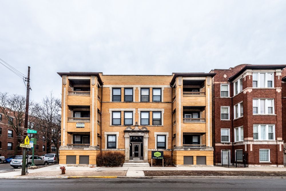 Yellow brick apartment building with balconies, sidewalk, street, and cloudy sky.