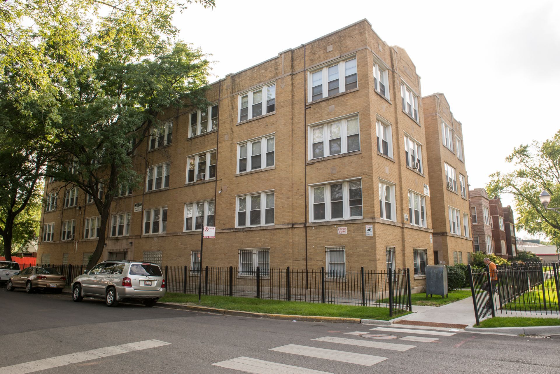 Multi-story brick apartment building on a city street, small cars parked nearby.