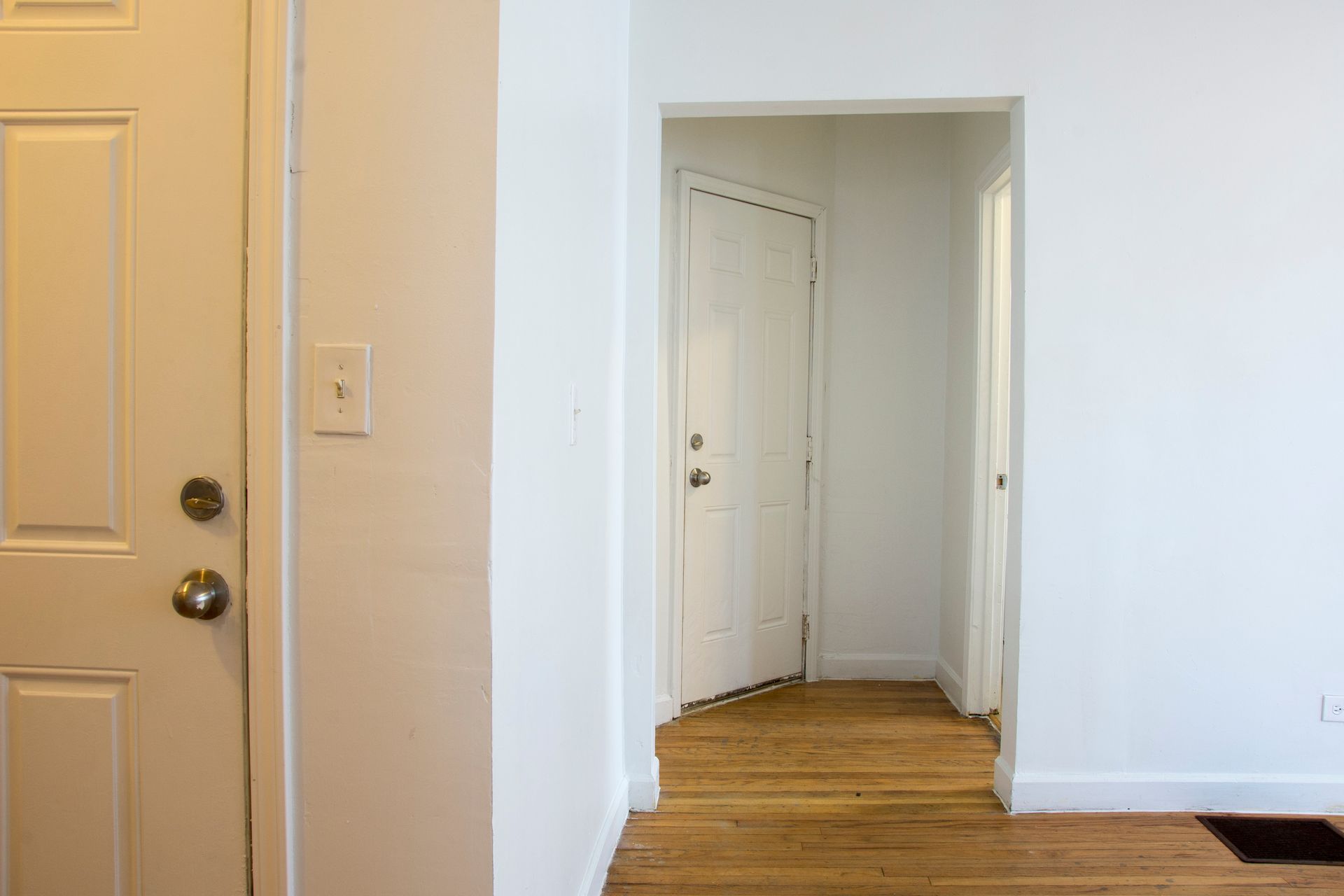 White interior, doorway to a hallway, door on the left, light switch.