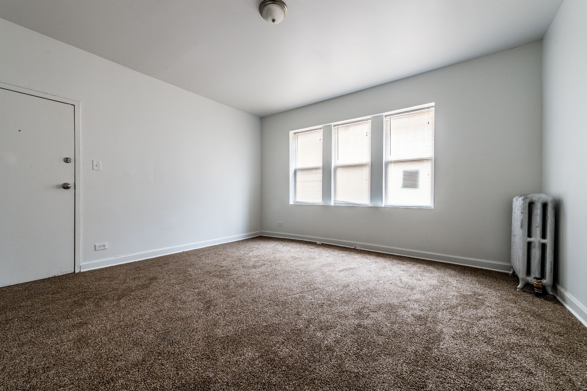Empty room with brown carpet, white walls, and a window with blinds.