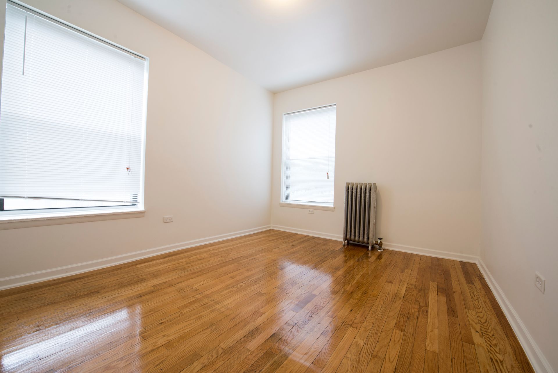 Empty room with hardwood floors, two windows, and a radiator.
