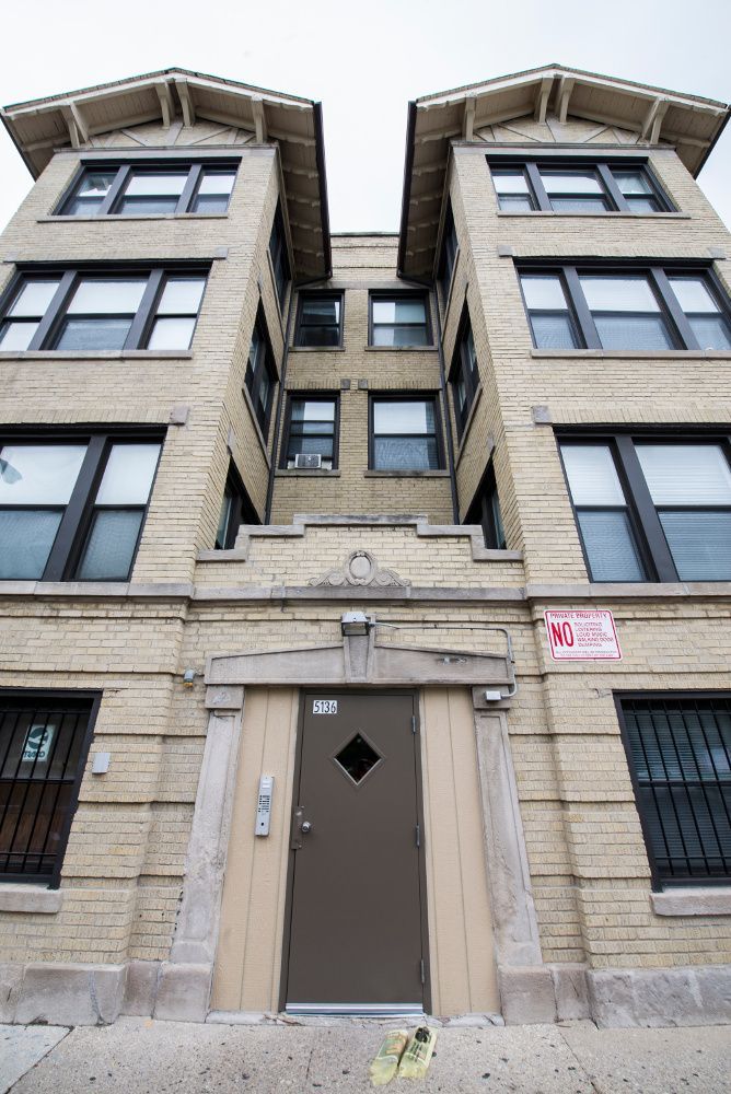 Beige brick apartment building with brown door, black-framed windows, and decorative roof peaks.