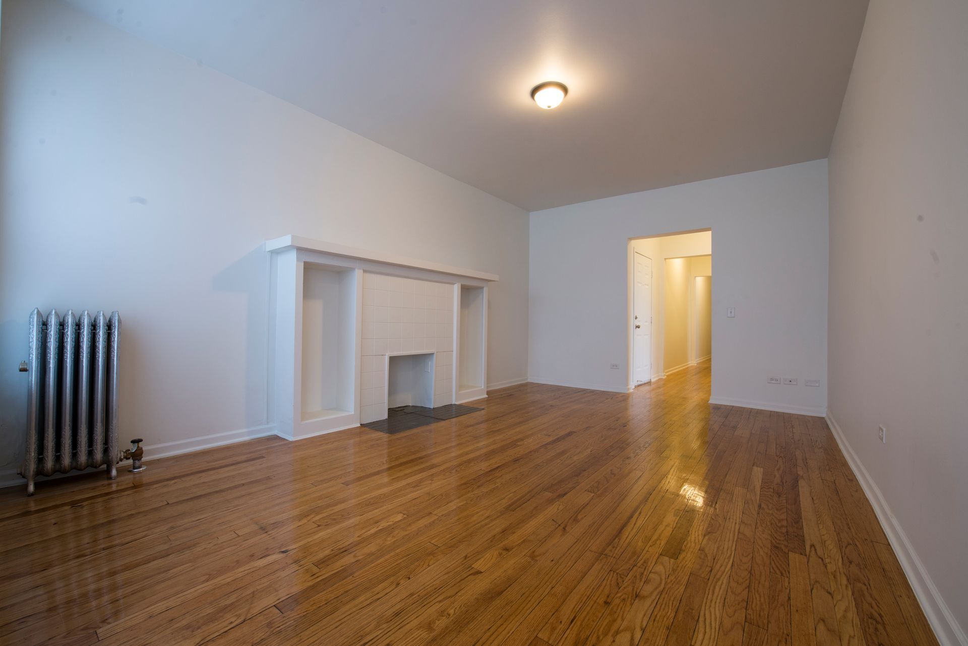 Empty living room with wood floor, radiator, fireplace, and doorway.