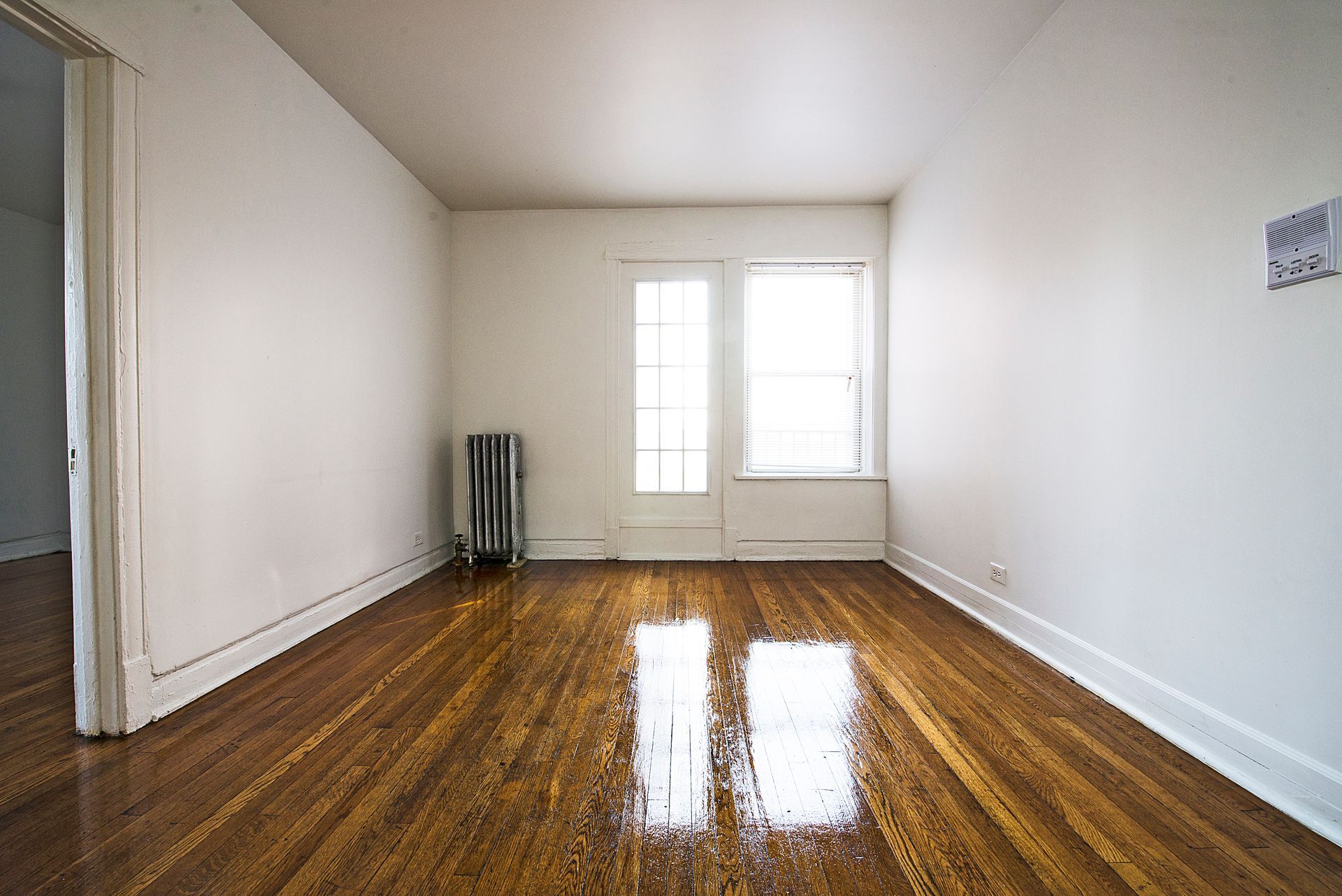 Empty room with hardwood floors, white walls, and a window.