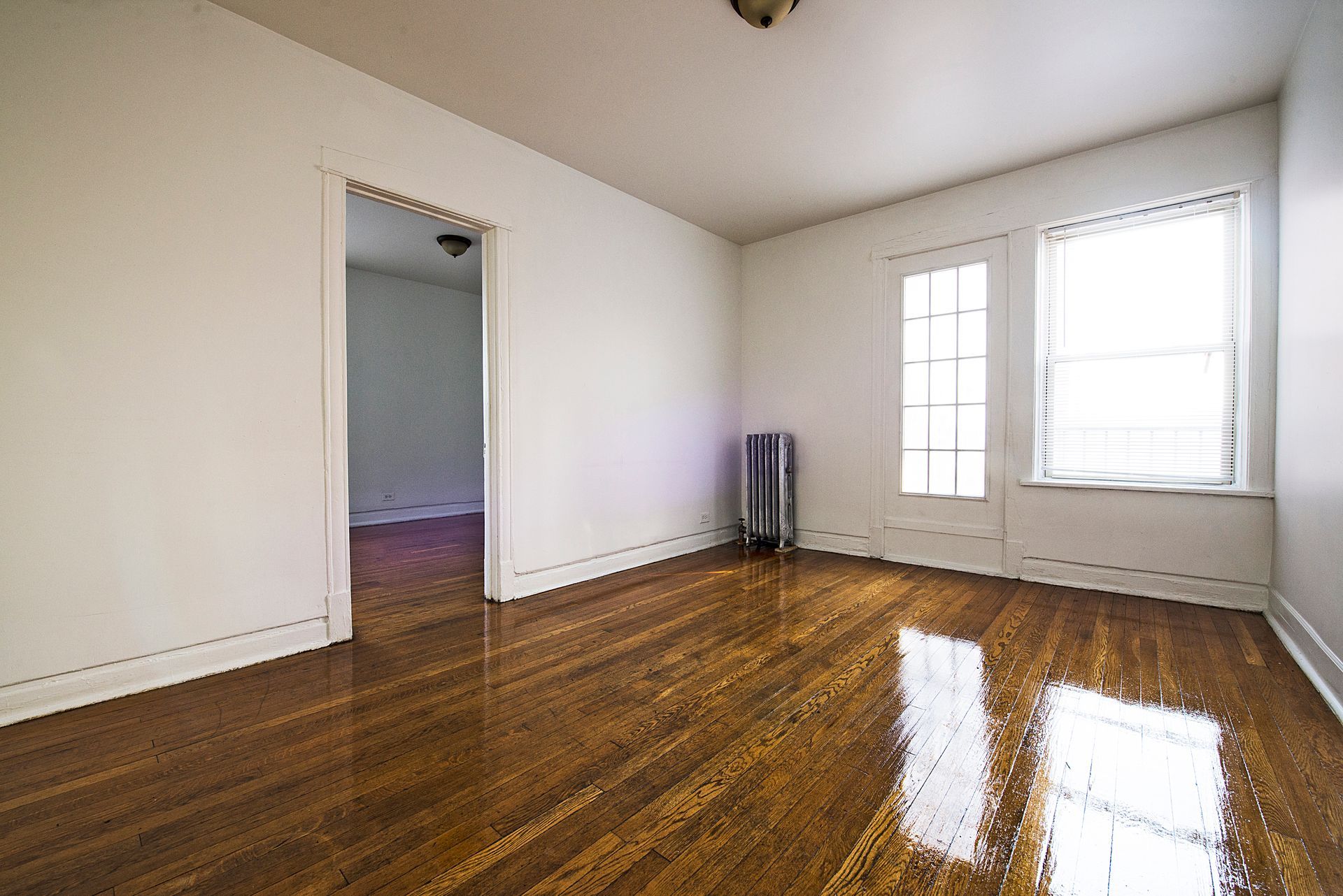 Empty room with hardwood floors, white walls, two windows, and an open doorway.