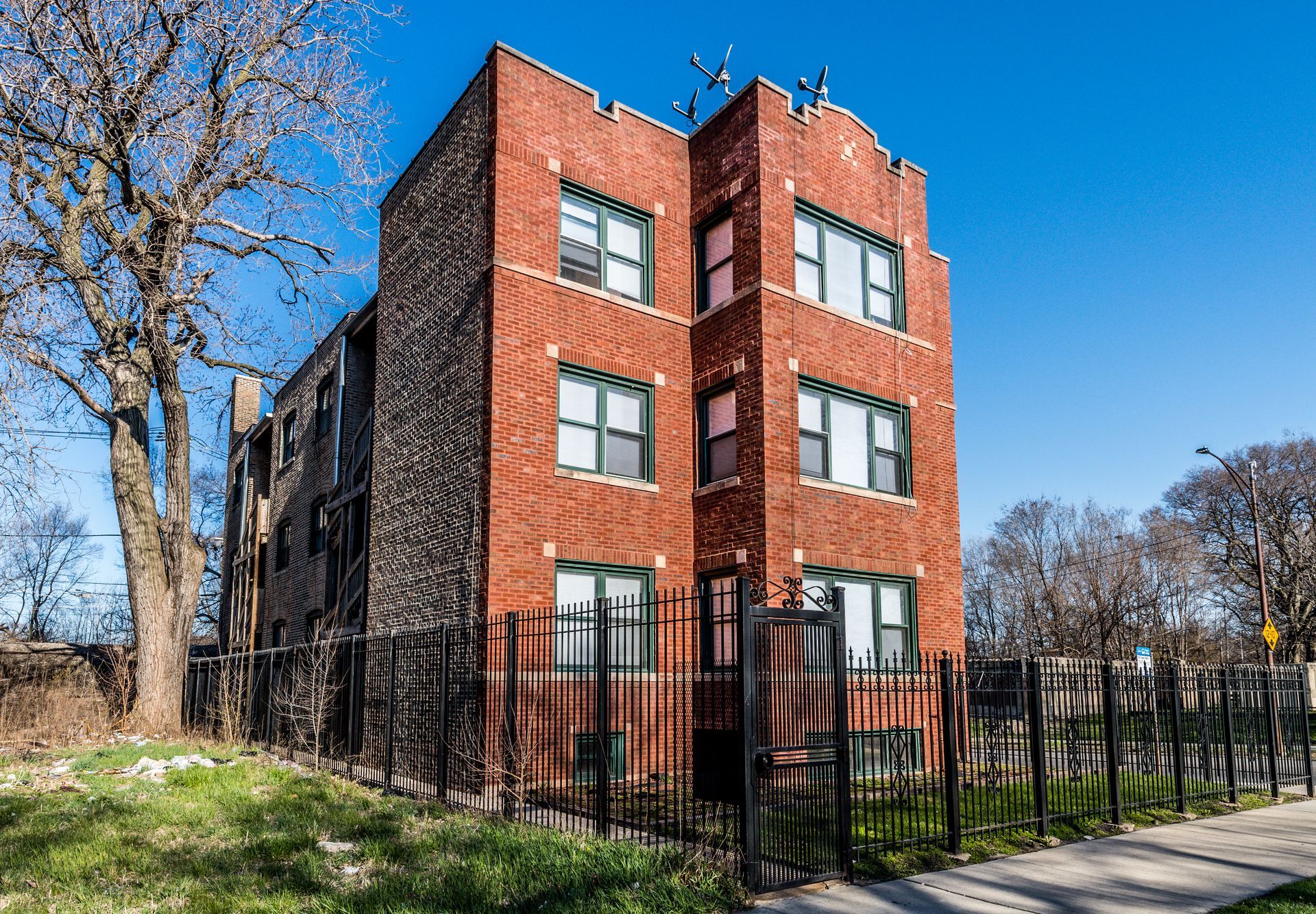 Red brick apartment building with black fence on a sunny day.