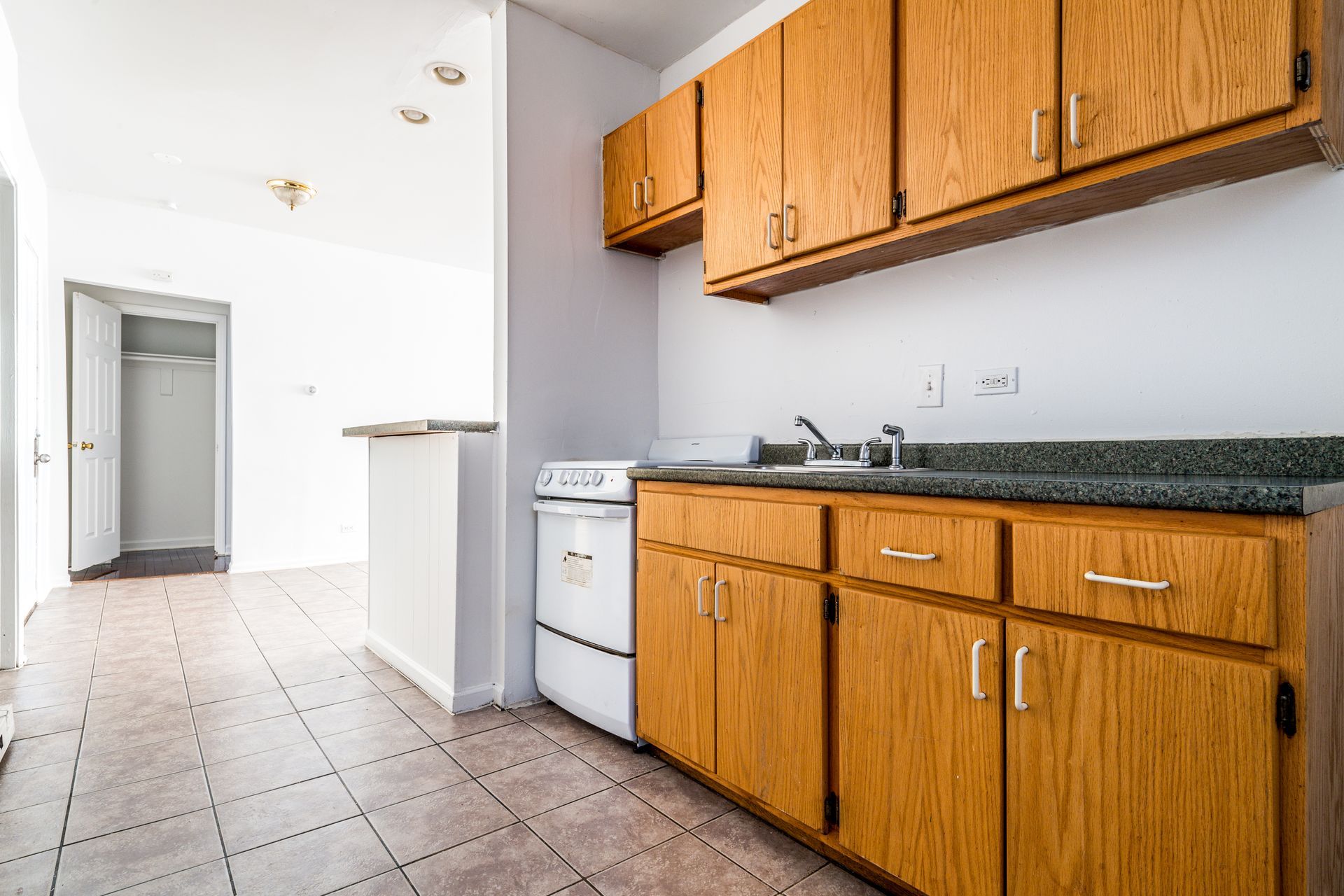 Kitchen with wooden cabinets, white appliances, and gray countertop. Tiled floor.