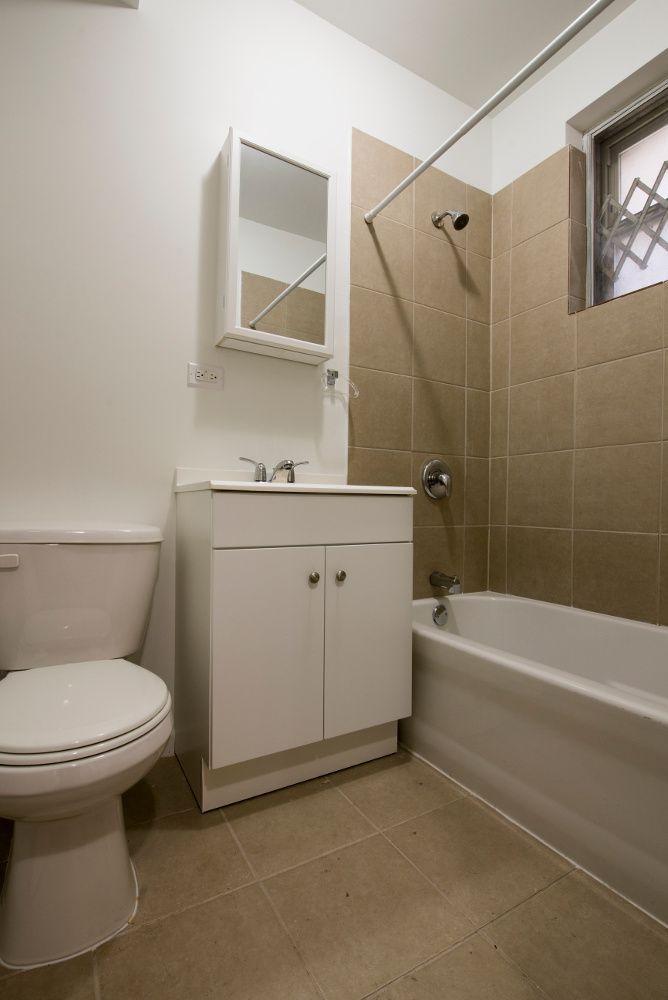 Bathroom with a white toilet, vanity, and bathtub; beige tile walls and floor.
