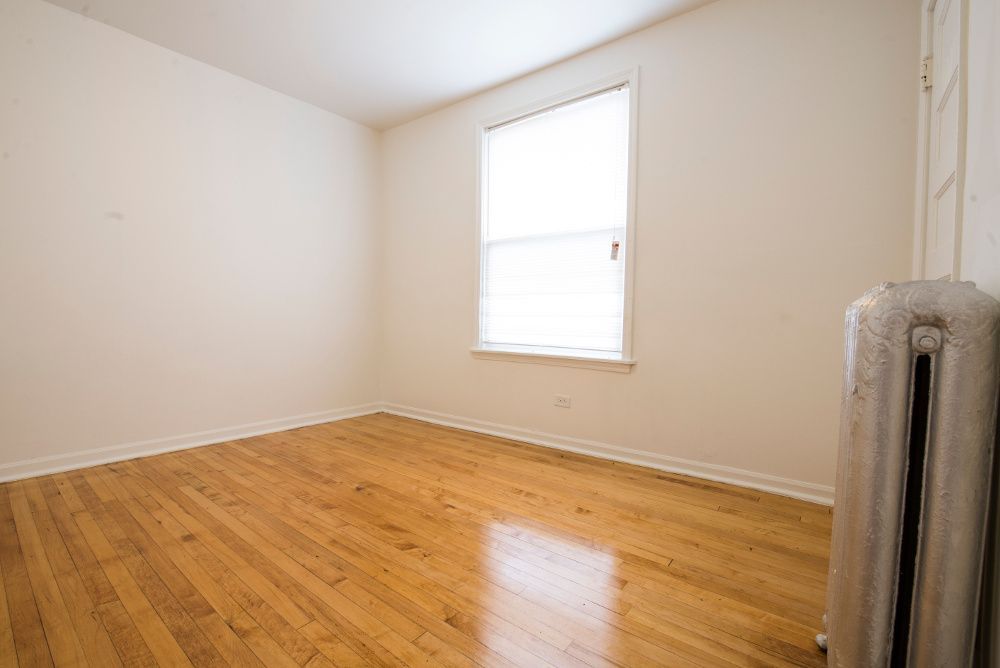 Empty room with hardwood floors, a window, and a radiator.