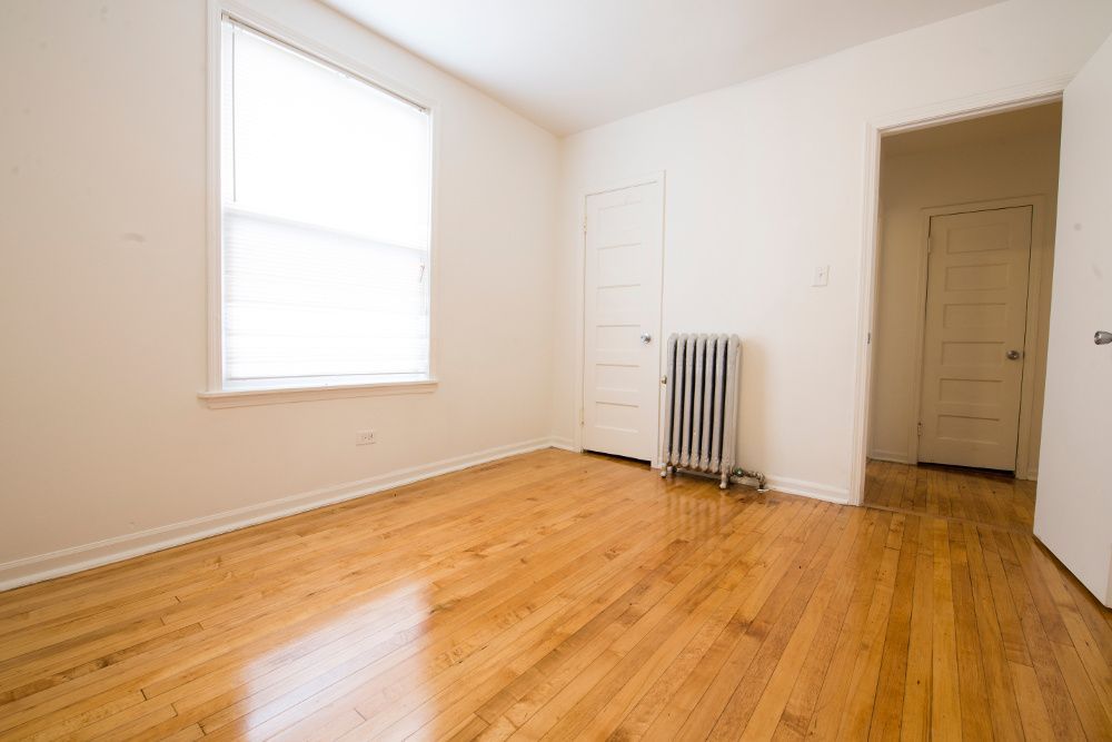 Empty room with hardwood floors, a window, doors, and a radiator.
