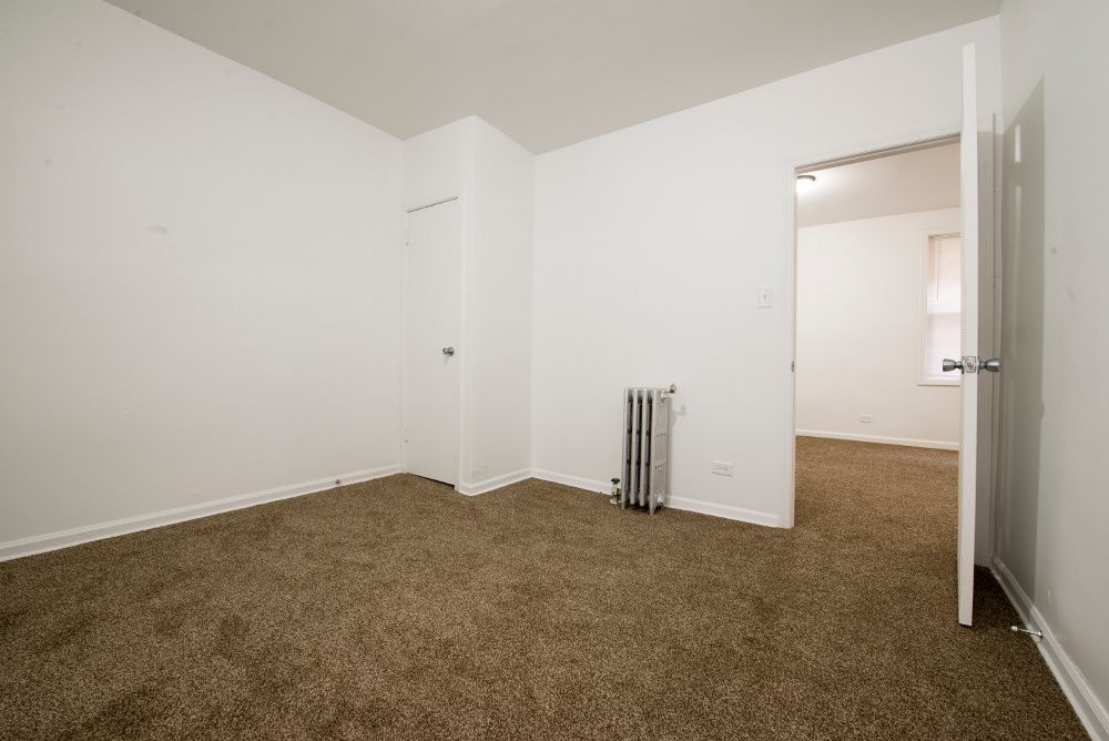 Empty room with brown carpet, white walls, closed door, and doorway to another room.