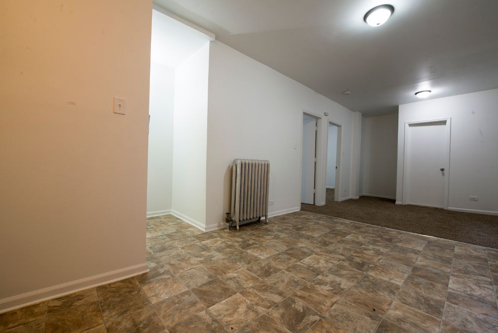 Empty apartment hallway with tile floor, radiator, doors, and overhead lighting.