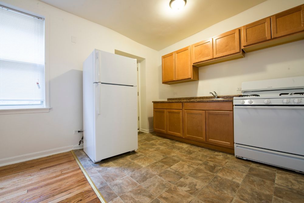 Kitchen with white appliances, wooden cabinets, and brown floor, near a window.