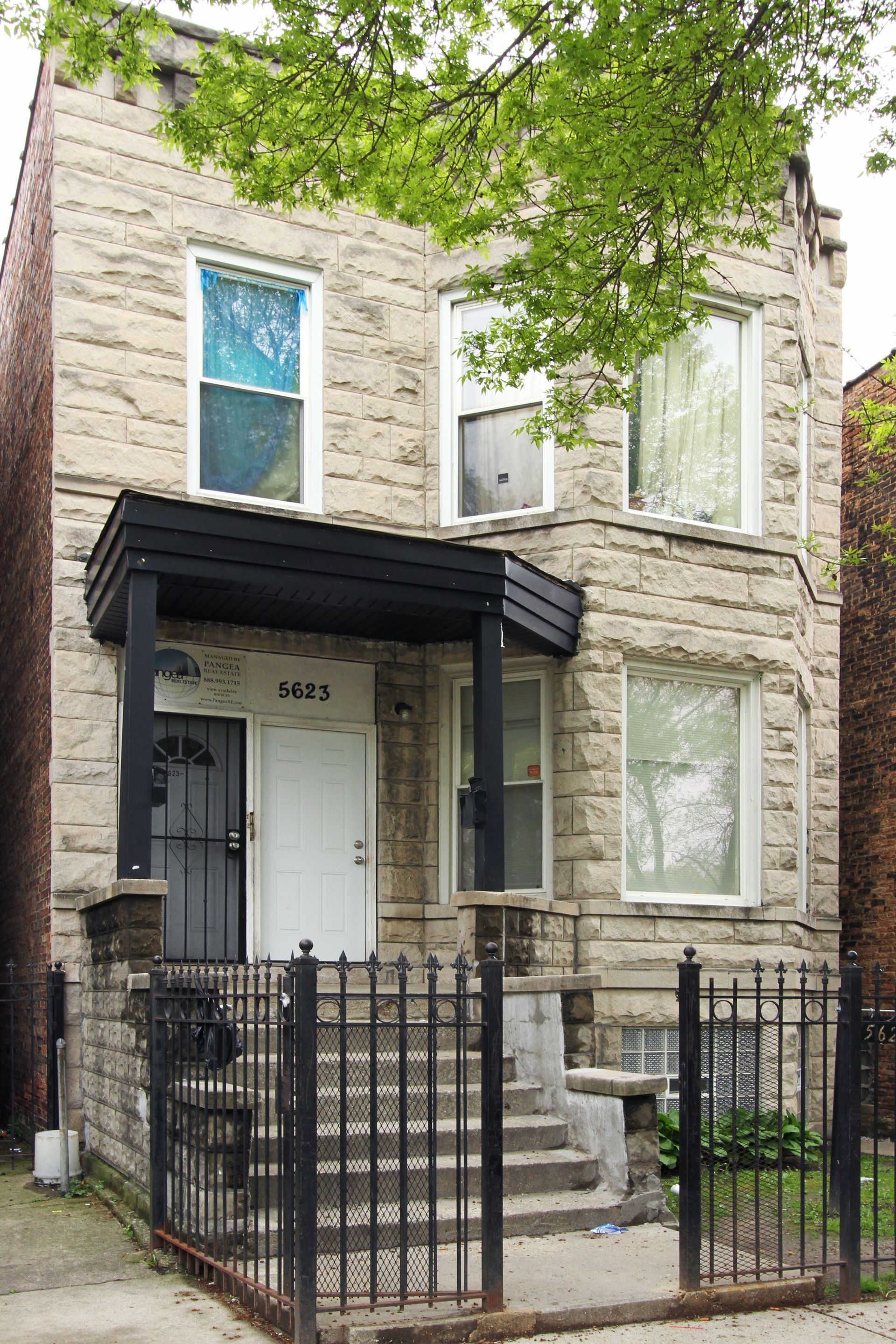 Two-story stone building with a porch, black railing, and iron gate in front.