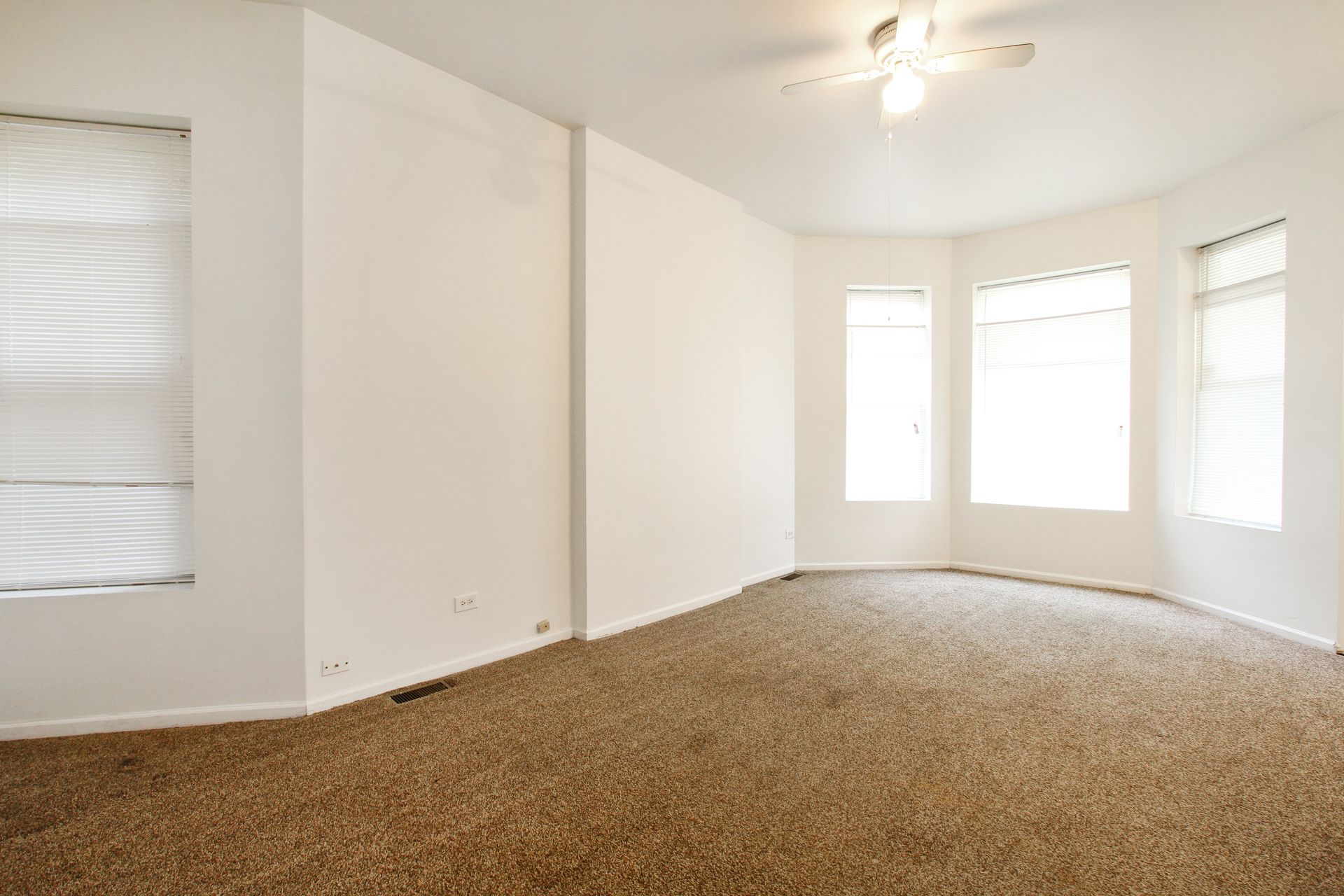 Empty room with beige carpet, white walls, and windows with blinds.
