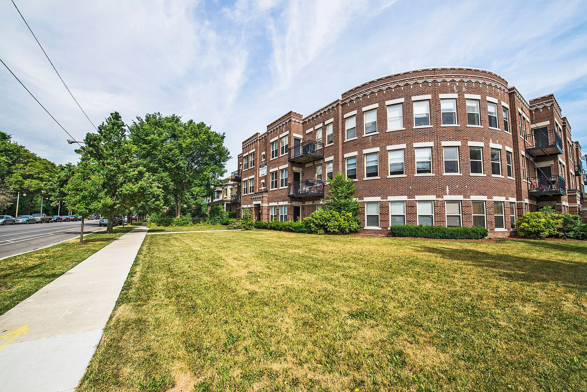 Brick apartment building with grassy lawn and sidewalk. Blue sky with clouds.